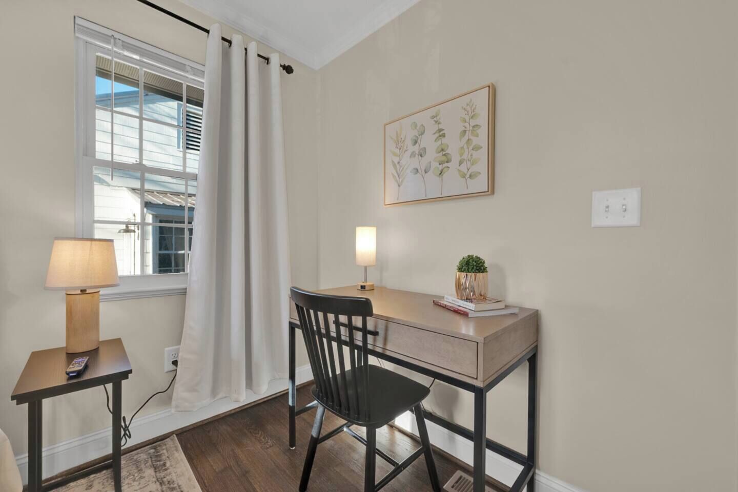 A room with a desk, chair, lamp, and a window with curtains.