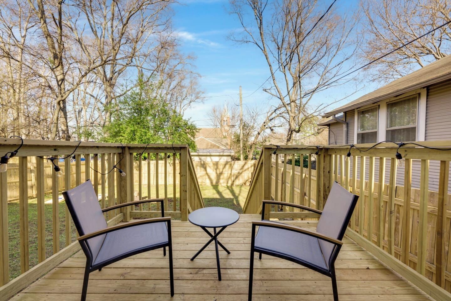A wooden deck with two chairs and a small table, surrounded by a wooden fence.
