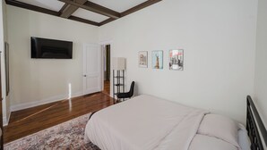 Un dormitorio con cama, televisor de pantalla plana en la pared, una puerta y una lámpara de pie.