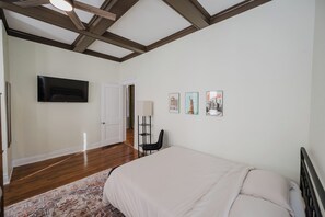 A bedroom with a bed, a flat-screen TV mounted on the wall, a door, and a floor lamp. - Vulcan Heights - Historic Home with Modern Touches (Birmingham)