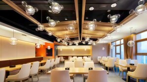 Uma área de jantar moderna com mesas e cadeiras redondas, teto alto com luminárias esféricas e janelas amplas com cortinas.