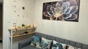 Ein Wohnzimmer mit grauem Sofa, Dekokissen, einem Wandbild und einer Deckenleuchte.