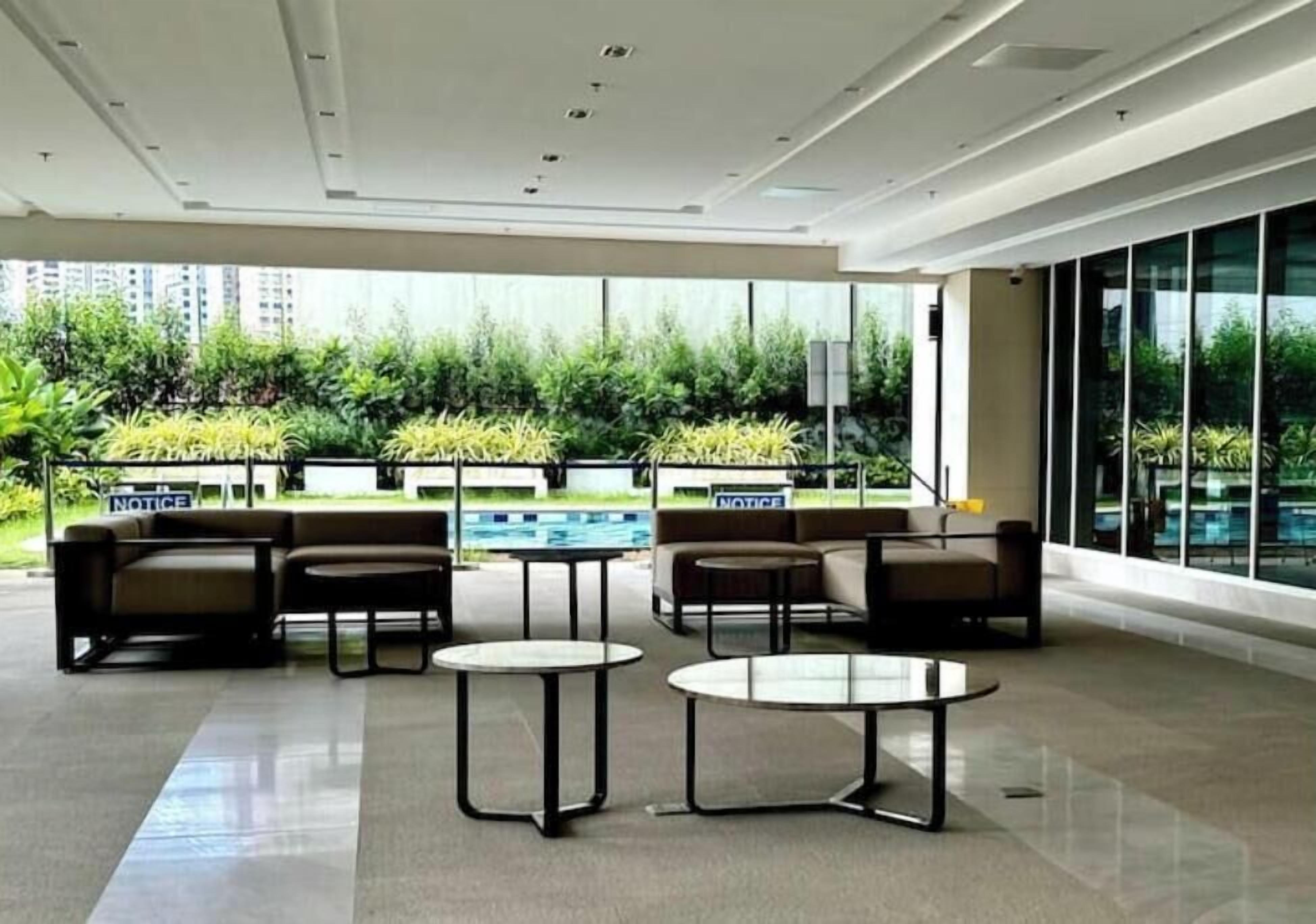 A modern lounge area with seating and tables, large windows, and a view of greenery outside.
