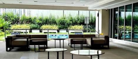 A modern lounge area with seating and tables, large windows, and a view of greenery outside.