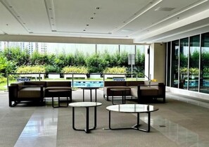 A modern lounge area with seating and tables, large windows, and a view of greenery outside. - The GoodVibes Condotel Red Residences Makati (Makati)