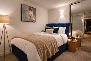 A modern bedroom with a tufted headboard, a large abstract painting, a floor lamp, and a bedside table with a mirror and decorative items. - CBD Apartment | Cozy Outdoor Balcony Setup, Heated Pool, Gym, Sauna and Dining (Melbourne)