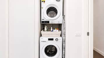 A compact, wall-mounted washer and dryer unit with a control panel and a basket of laundry supplies.