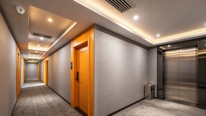 Ein Hotelgang mit Teppichböden, Holztüren und einem modernen Aufzug.