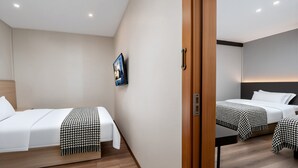 Ein Hotelzimmer mit zwei Betten, Holzboden und einem an der Wand befestigten Fernseher.