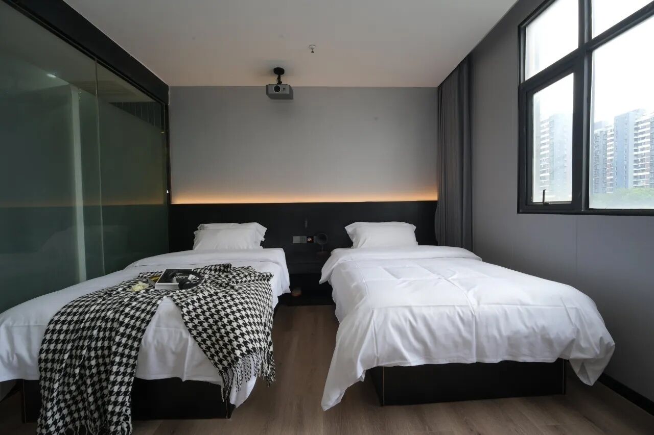 Een hotelkamer met twee bedden, een projector aan het plafond en een groot raam.