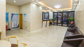Eine Hotelhalle mit Empfangsschalter, einer Sitzecke und Informationsplakaten an den Wänden.