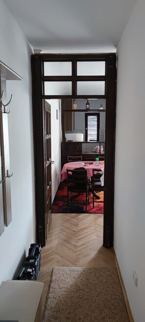 Ein Flur, der in einen Essbereich mit Tisch und Stühlen führt, mit Holzboden und einem Fenster mit Jalousien.