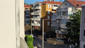 En balkong med utsikt över en bostadsgata, en byggnad med ett rött tak och en klarblå himmel.