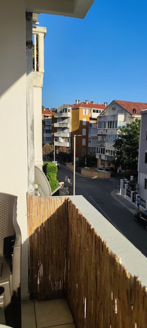 Ein Balkon mit Blick auf eine Wohnstraße, ein Gebäude mit rotem Dach und einem strahlend blauen Himmel.