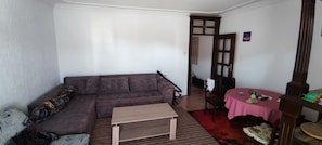 Ein Wohnzimmer mit einer Couch, einem kleinen Tisch, einem Sessel und einem Esstisch mit rotem Karomuster.