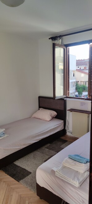 Ein kleines Zimmer mit einem Einzelbett, einem Fenster, einem Heizkörper und einem Hinweis zum Schließen der Jalousien bei Regen.
