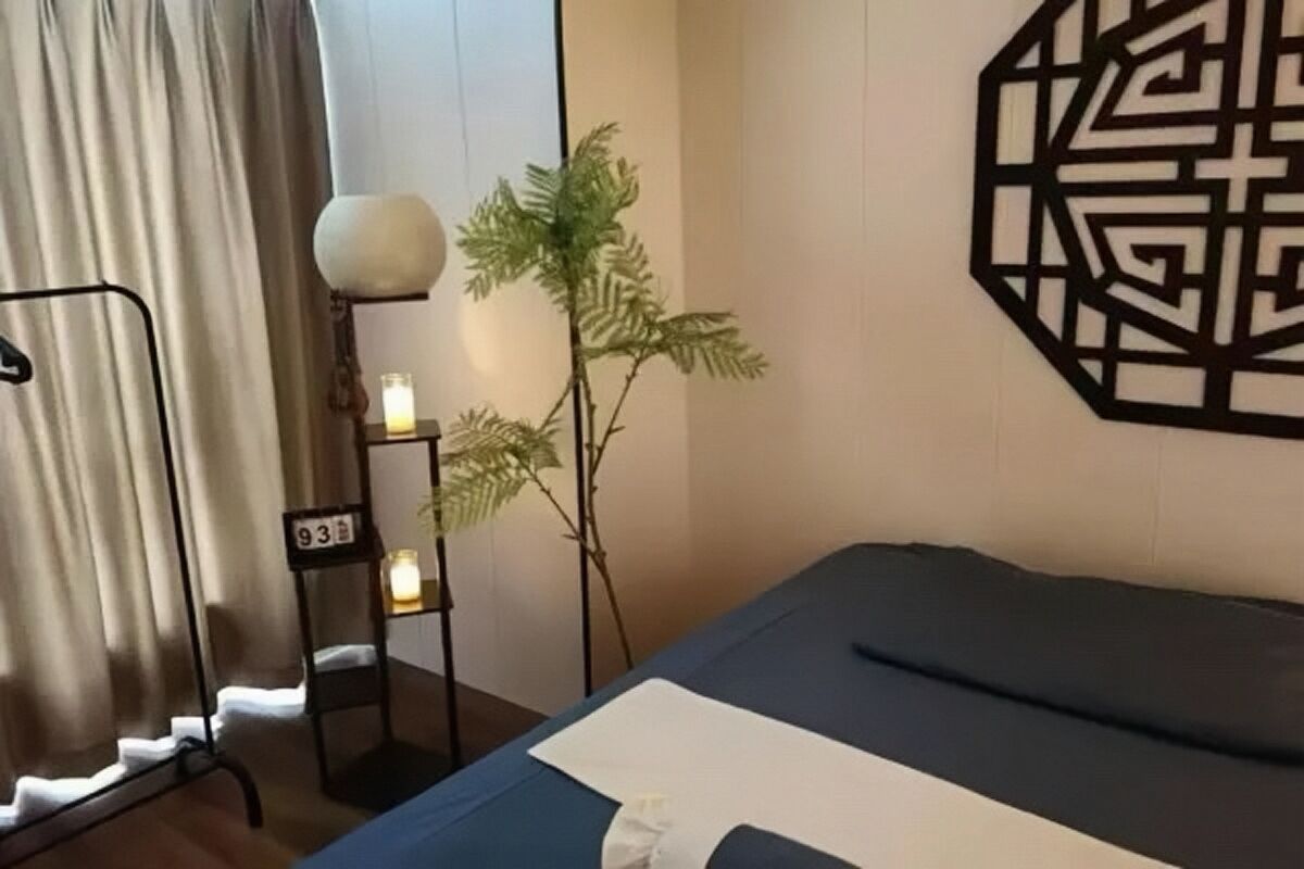 Habitación de hotel con cama, cortinas, un adorno geométrico en la pared, una mesita con lámpara y una planta en maceta.