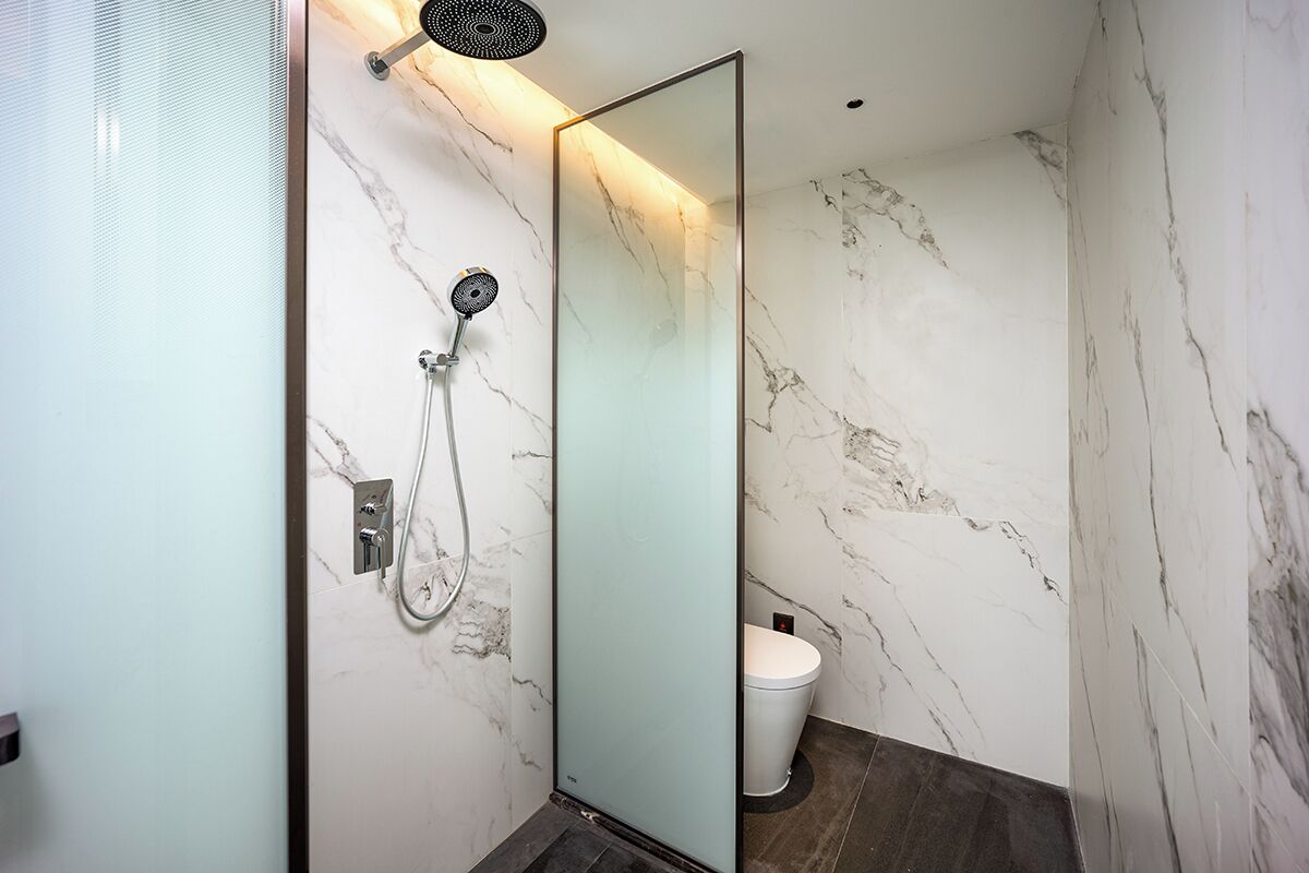 Baño con cabina de ducha de vidrio, inodoro y paredes de mármol.
