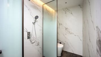 Baño con cabina de ducha de vidrio, inodoro y paredes de mármol.