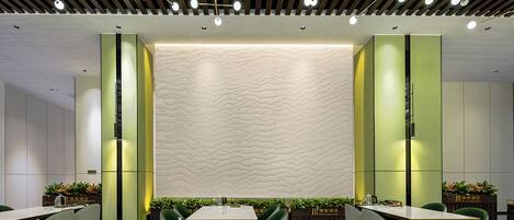 A modern dining area with a central table, green chairs, and a patterned wall.