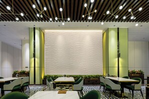A modern dining area with a central table, green chairs, and a patterned wall. - Mehood Elegant Intl. Nanhai Guangfo (Foshan)