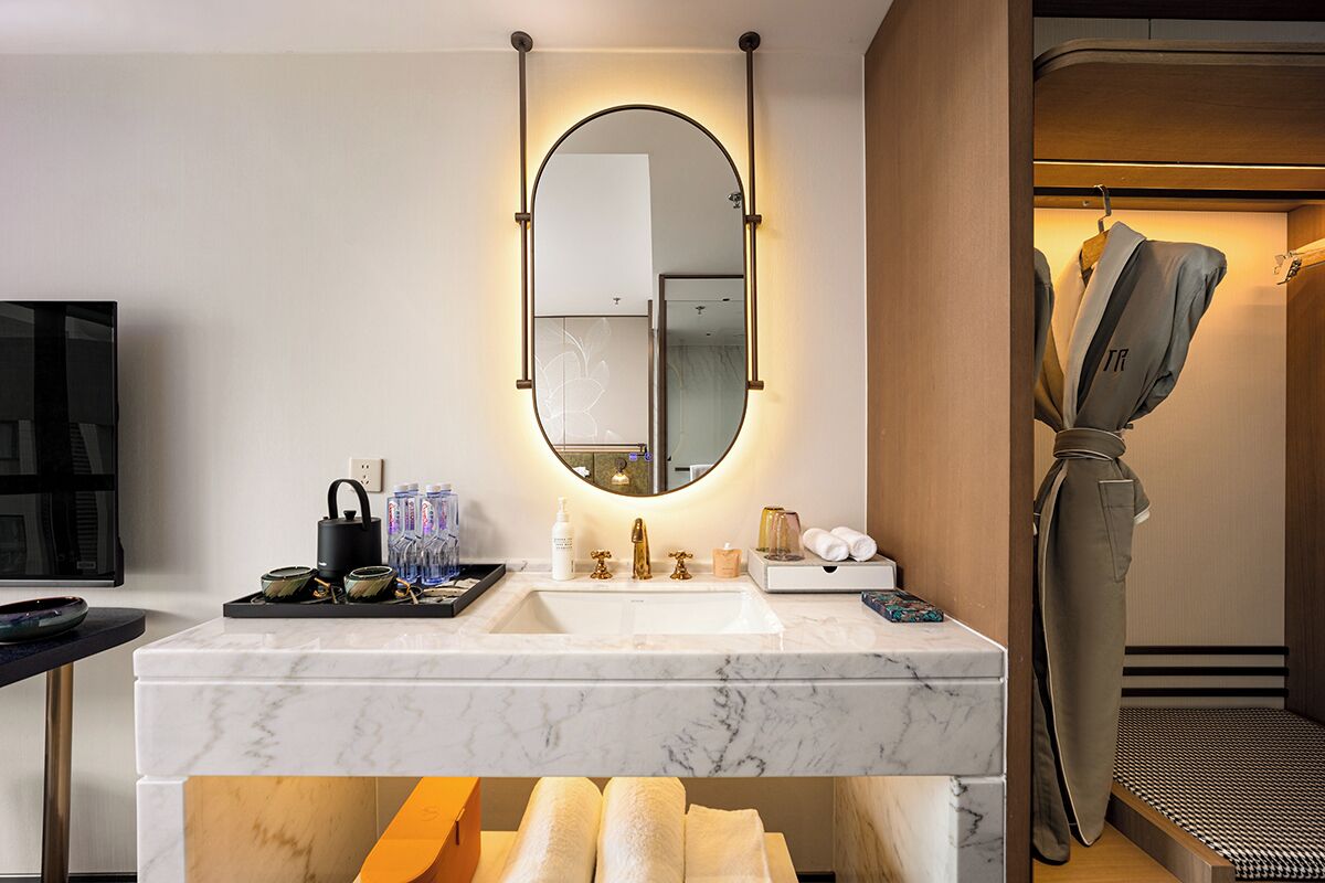 Un baño moderno con lavamanos de mármol, un espejo grande y un perchero para toallas.