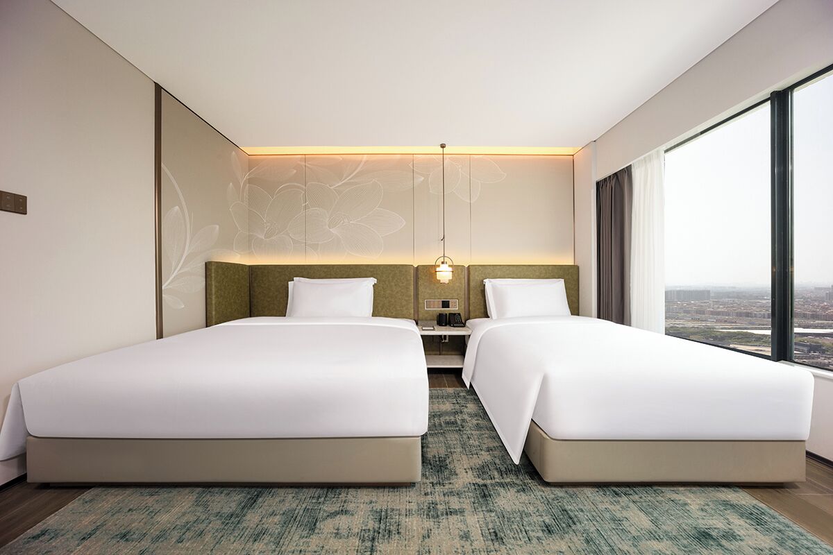 Habitación de hotel moderna con dos camas, una mesita de noche y vistas a la ciudad.