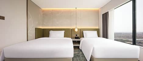 Habitación de hotel moderna con dos camas, una mesita de noche y vistas a la ciudad.