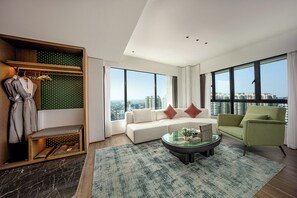A modern living room with a sofa, a green armchair, a coffee table, and a view of the city through large windows. - Mehood Elegant Intl. Nanhai Guangfo (Foshan)