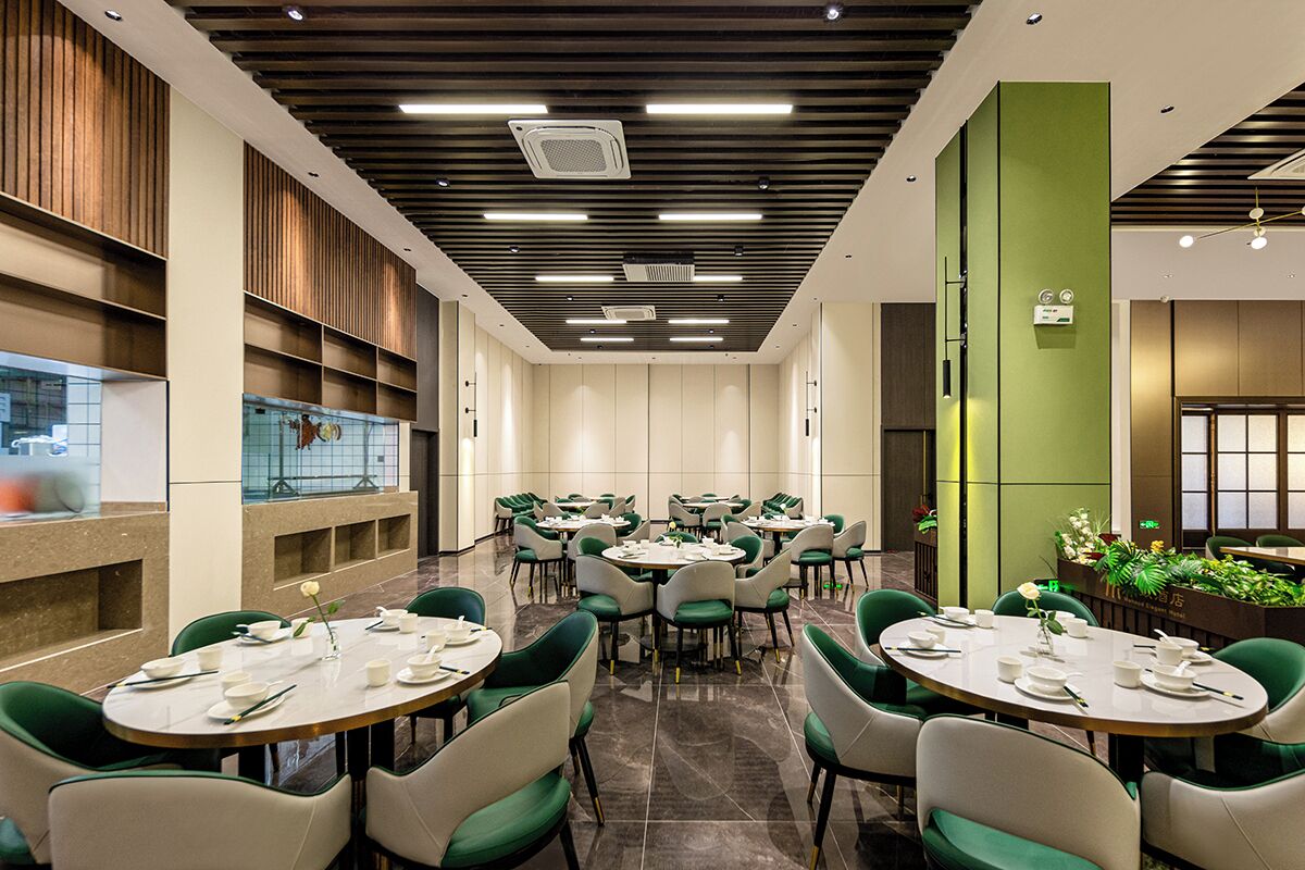 Un comedor con mesas redondas y sillas verdes, con vajilla blanca.