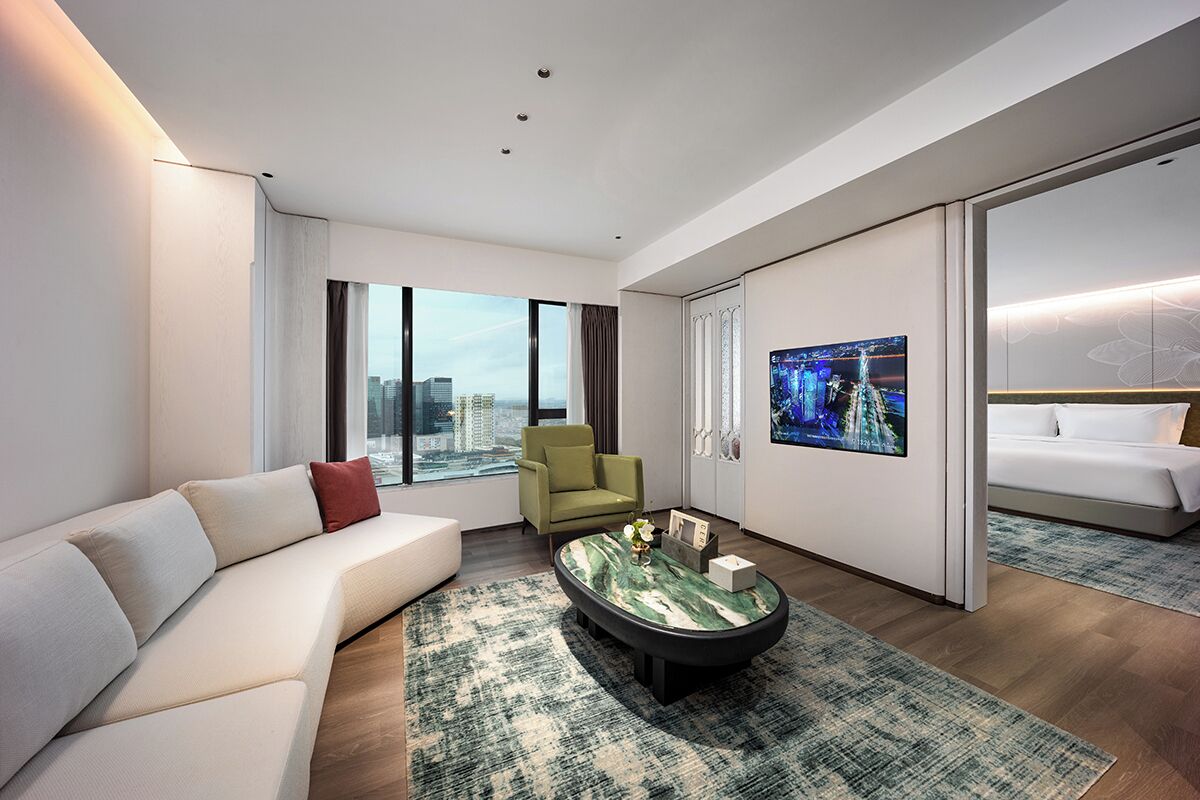 A modern hotel room with a sofa, armchair, and a bed.
