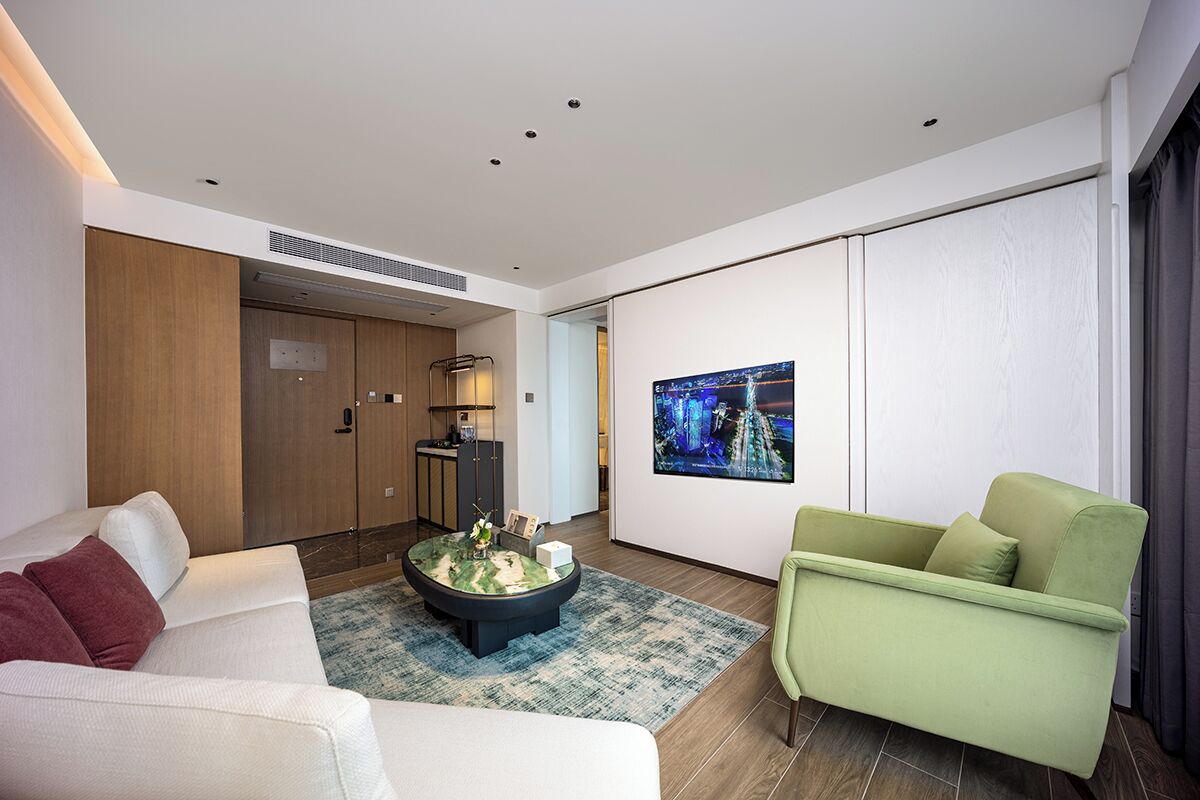 Una sala moderna con un sofá, un sillón verde, una mesa de centro y un televisor de pantalla plana montado en la pared.