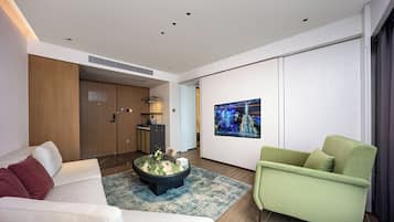 Una sala moderna con un sofá, un sillón verde, una mesa de centro y un televisor de pantalla plana montado en la pared.
