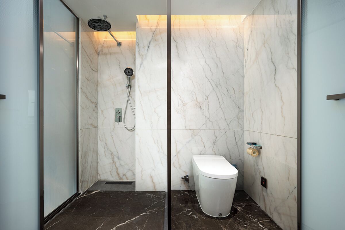 A modern bathroom with a glass shower enclosure, marble walls, and a toilet.