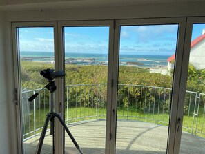A balcony with a telescope, a view of the sea, and a distant bridge.