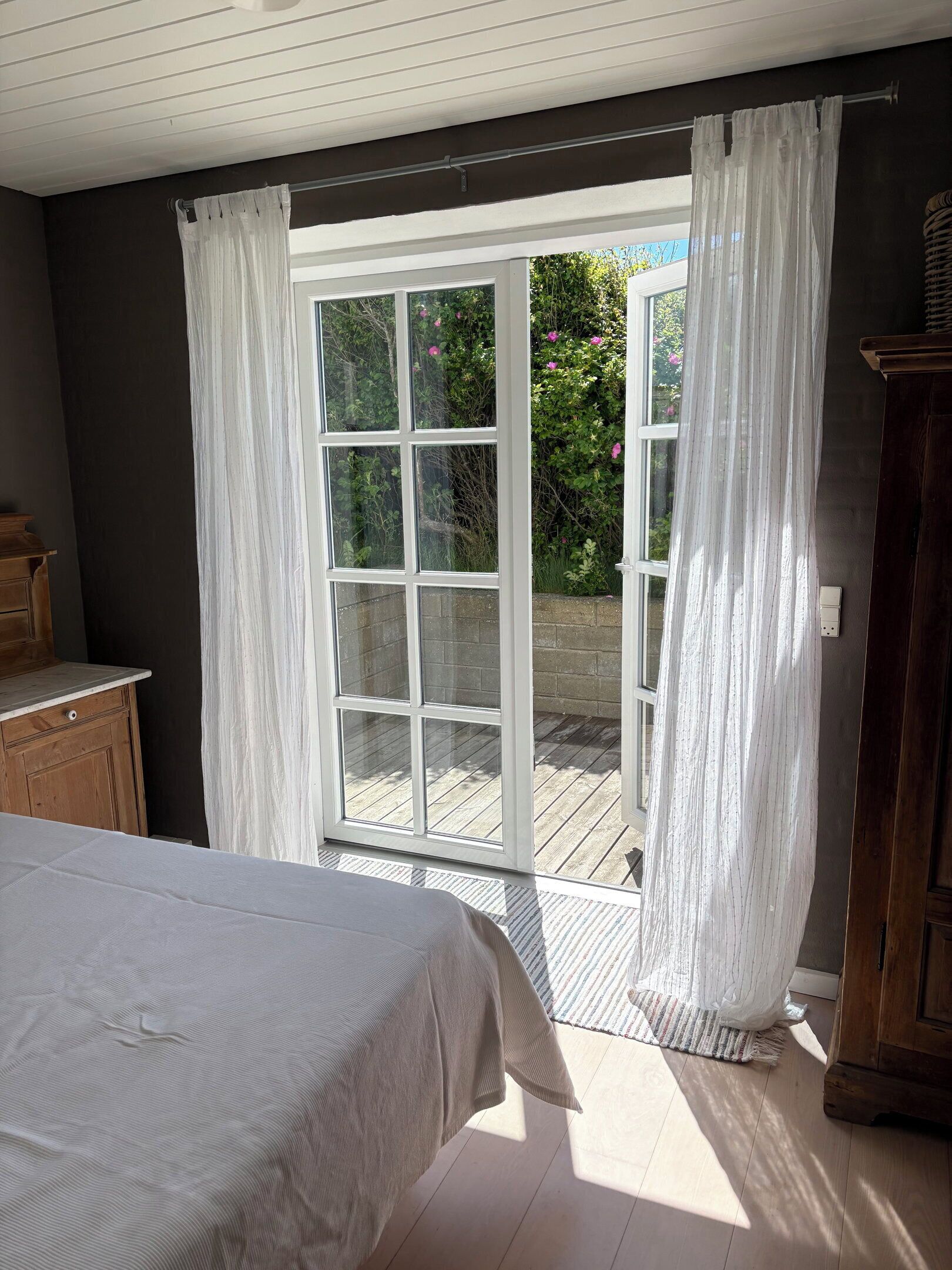 Une chambre à coucher comprenant un lit, une commode en bois et une porte-fenêtre coulissante donnant sur un espace extérieur.