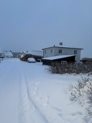 A snow-covered residential street with houses and a car parked on the side.