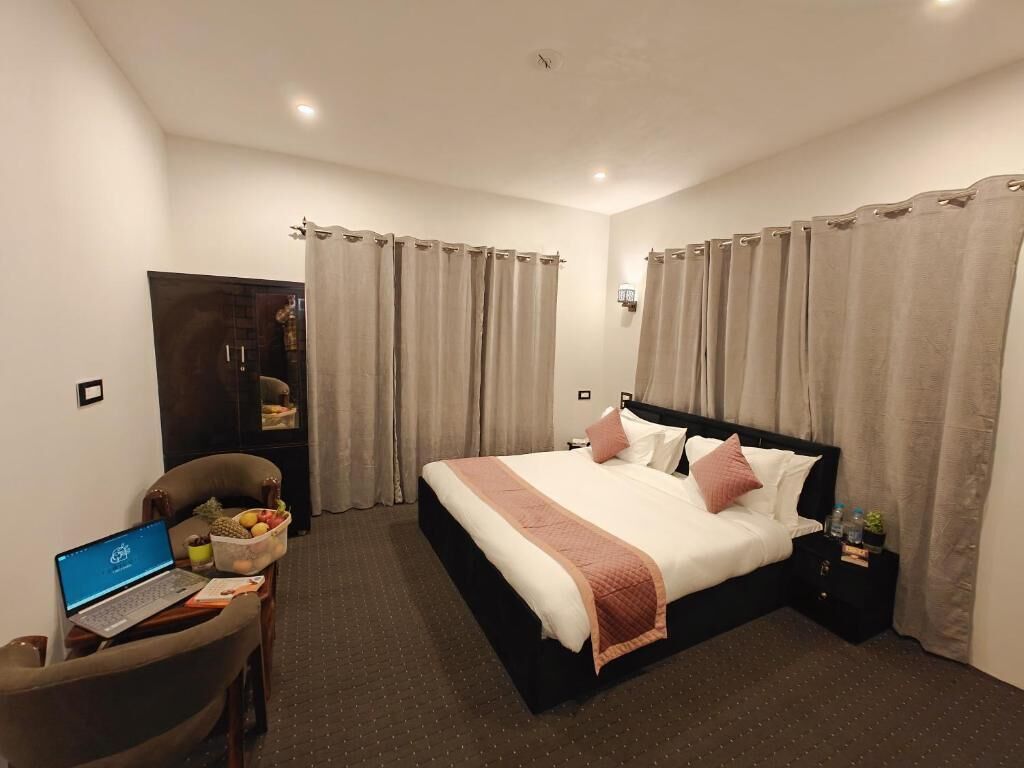 Habitación de hotel con una cama, un escritorio con una computadora portátil, una silla y una mesita con fruta.
