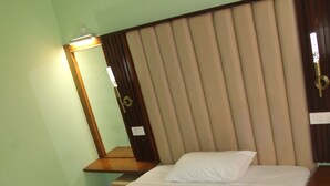 Una cama bien hecha con edredón y almohadas blancos, cabecera de madera, mesita de noche con lámpara y espejo en la pared.