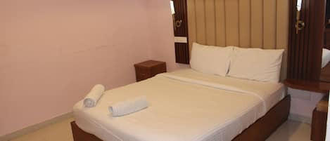 A hotel room with a large bed, a wooden headboard, a nightstand, and a wall-mounted light fixture.