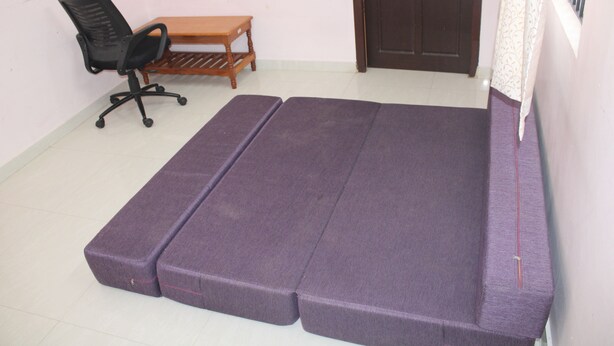 Una habitación con una cama, una silla, una mesita y una puerta.