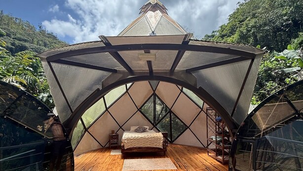 A hexagonal tent with a wooden deck, a bed, and a small table. - Unique 2 Story Dome (Rivas)