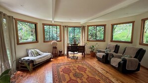 A spacious living room with a large wooden floor, a patterned rug, and multiple windows offering a view of greenery. - Unique 2 Story Dome (Rivas)