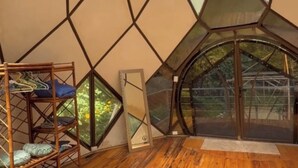 A room with a geometric ceiling design, wooden flooring, a white rug, and a glass door leading outside. - Unique 2 Story Dome (Rivas)