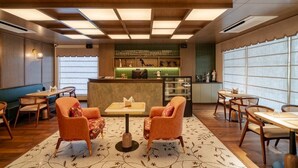 A hotel lobby with wooden flooring, a reception desk, seating areas, and large windows. - AKS Palace (Varanasi)