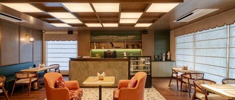 A hotel lobby with wooden flooring, a reception desk, seating areas, and large windows.