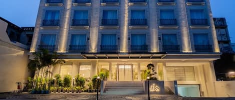 A multi-story hotel with a central entrance, balconies, and a well-lit facade.