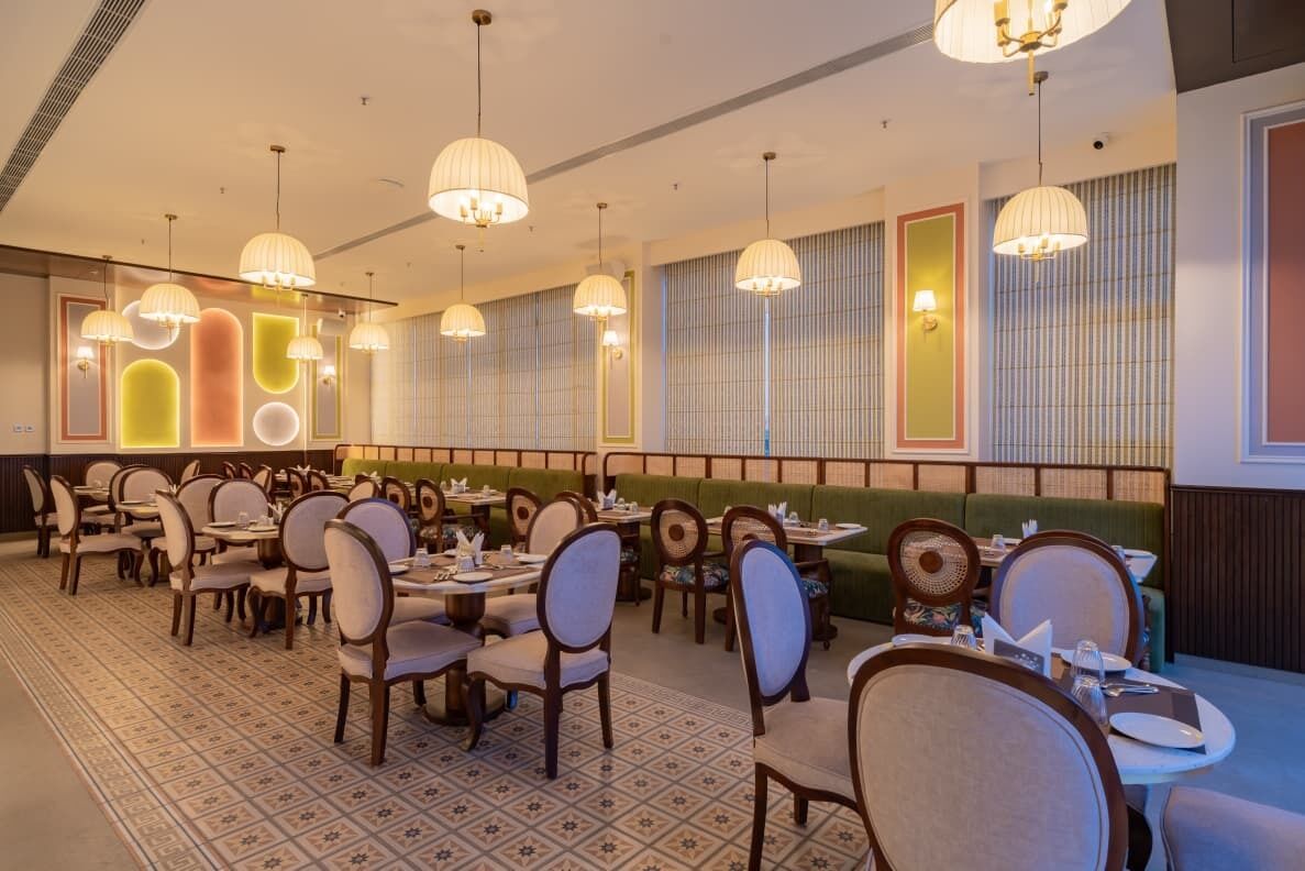 A restaurant with multiple dining tables and chairs, pendant lighting, and a patterned floor.