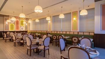 A restaurant with multiple dining tables and chairs, pendant lighting, and a patterned floor.