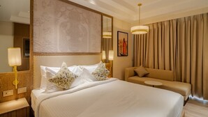 A hotel room with a large bed, a sofa, a small table, and a large window with curtains. - AKS Palace (Varanasi)